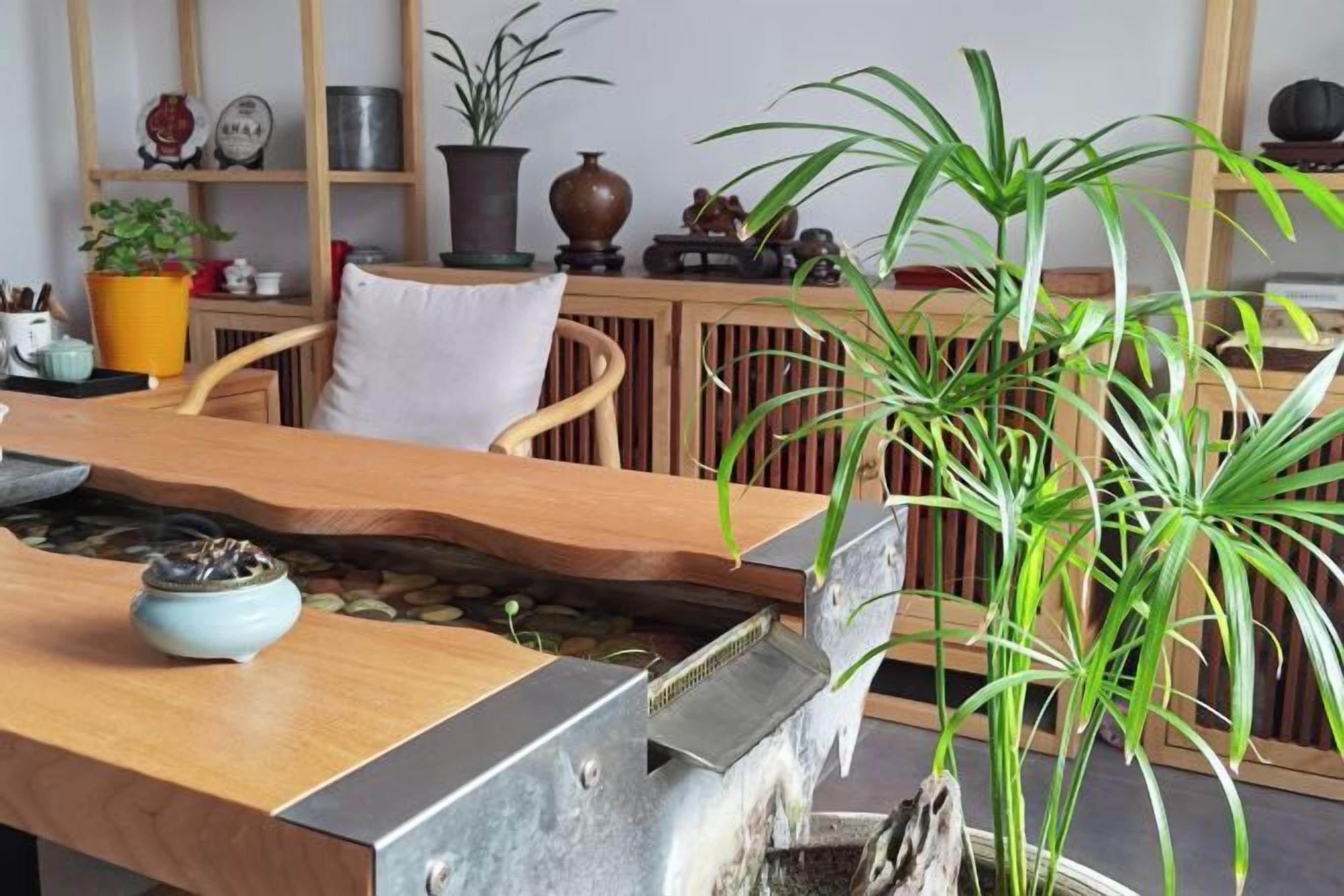 Mesa de jantar de madeira com um recurso de água embutido, rodeada por cadeiras e plantas em vasos.