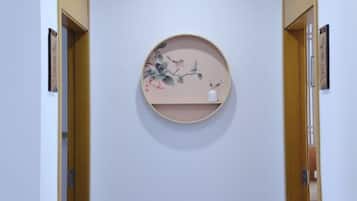 Corredor com prateleira redonda fixada na parede, exibindo uma obra de arte floral.