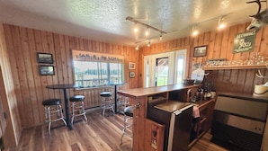 A kitchen with wooden walls, a bar area with stools, a refrigerator, and a window with a view of the outdoors. - Exclusive Mountain Grandeur!
Back door to the Seven Devils Mountain range (Council)