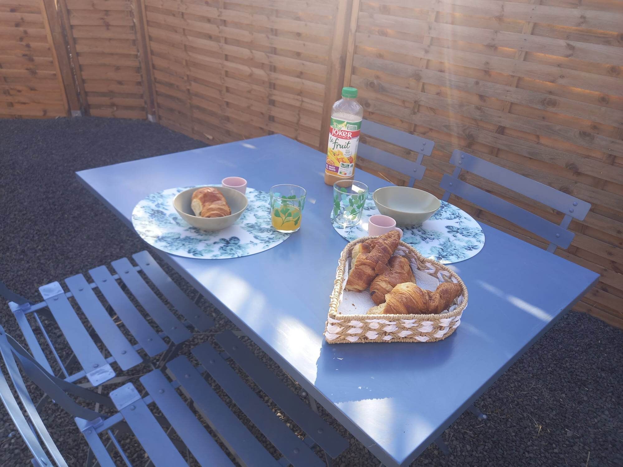 Una mesa con una cesta de cruasanes, una botella de jugo y un bol de fruta.