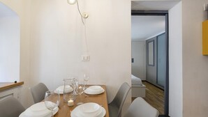 Een eetgedeelte met een houten tafel gedekt voor vier personen, witte borden, glazen en bestek. Boven de tafel hangt een lamp.