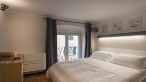 Een slaapkamer met een bed, een houten dressoir, een radiator en een balkon met gordijnen.