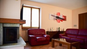 Un salon avec une cheminée, des canapés en cuir rouge, une table basse et une fenêtre avec des stores.