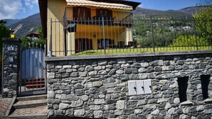 Un bâtiment à deux étages, avec un mur de pierre à l’avant, une clôture en métal et une chaîne de montagnes en arrière-plan.