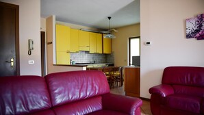 Un salon avec un canapé en cuir rouge et un fauteuil rouge, une cuisine avec des meubles jaunes et un coin repas avec des chaises en bois.