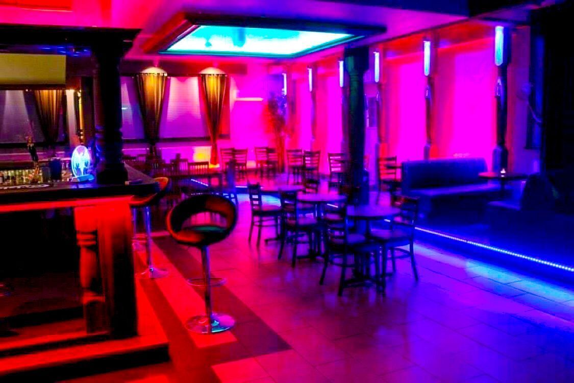 Una zona de bar con mostrador y taburetes, rodeada de mesas y sillas.