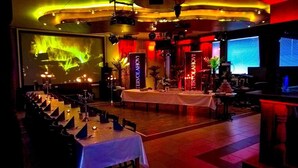 A banquet hall with tables set for a formal event, a large screen displaying a presentation, and ambient lighting. - ArcticMagic (Tervola)