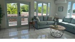 A spacious living room with a light blue sofa, a coffee table, and a view of greenery through large sliding doors. - The Enchanted Pearl come immerse yourself in relaxation and crystal clear waters (Vega Baja)