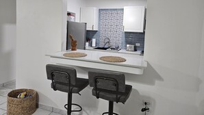 A compact kitchen with a white countertop, two bar stools, a refrigerator, a toaster, and a patterned backsplash. - The Enchanted Pearl come immerse yourself in relaxation and crystal clear waters (Vega Baja)