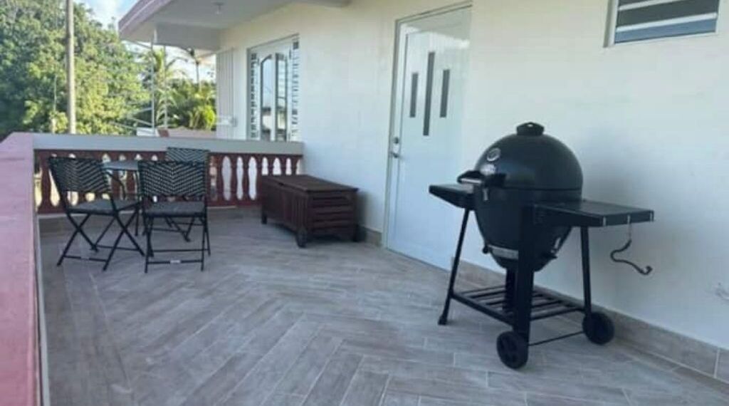 A covered patio with a barbecue grill, outdoor seating, and a door.