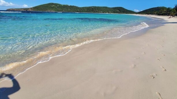 A beach with clear turquoise water, sandy shore, and green hills in the background. - The Enchanted Pearl come immerse yourself in relaxation and crystal clear waters (Vega Baja)