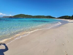 A beach with clear turquoise water, sandy shore, and green hills in the background. - The Enchanted Pearl come immerse yourself in relaxation and crystal clear waters (Vega Baja)
