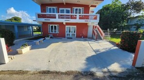 Un bâtiment à deux étages, doté d’une façade rouge et de bordures blanches, d’un balcon à l’étage supérieur et d’une allée pavée menant à l’entrée.