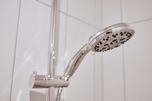 A showerhead with multiple nozzles, attached to a curved pipe, against a tiled wall.