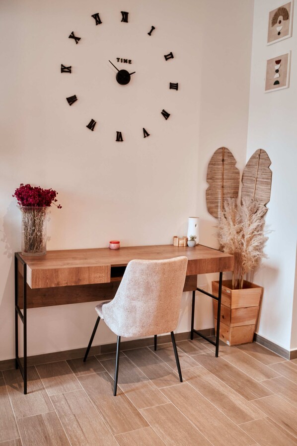 A wooden desk with a clock, a chair, a vase with flowers, and decorative leaves on the wall. - Narama (Guatemala City)