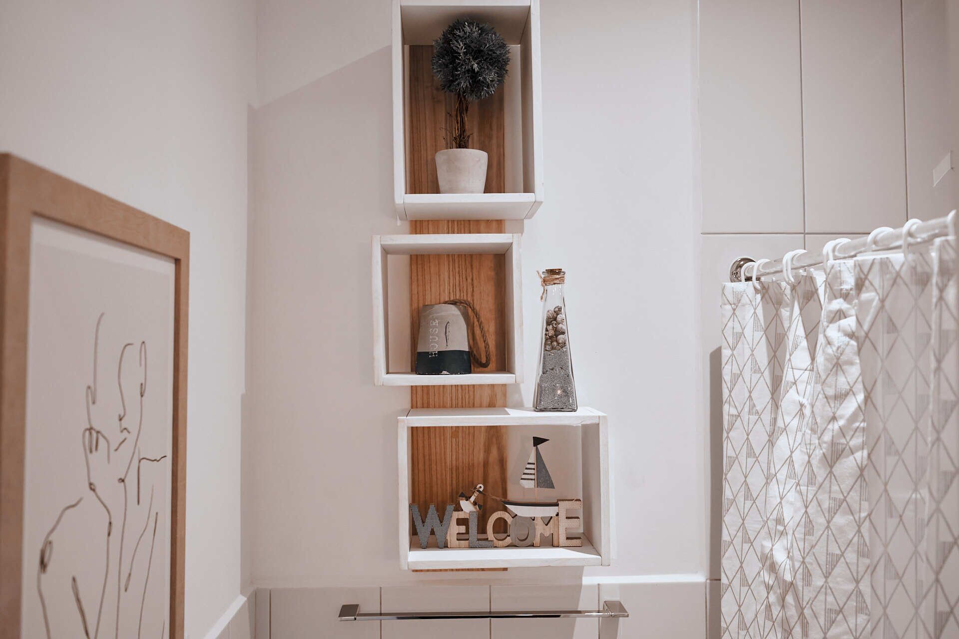 A bathroom with a white shower curtain, a towel rack, and a shelf with decorative items including a potted plant and a small figurine.
