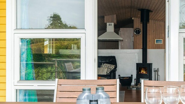Een gezellige kamer met een houten tafel, verrekijkers en wijnglazen. Een open haard is op de achtergrond te zien, en een raam biedt uitzicht op groen buiten.