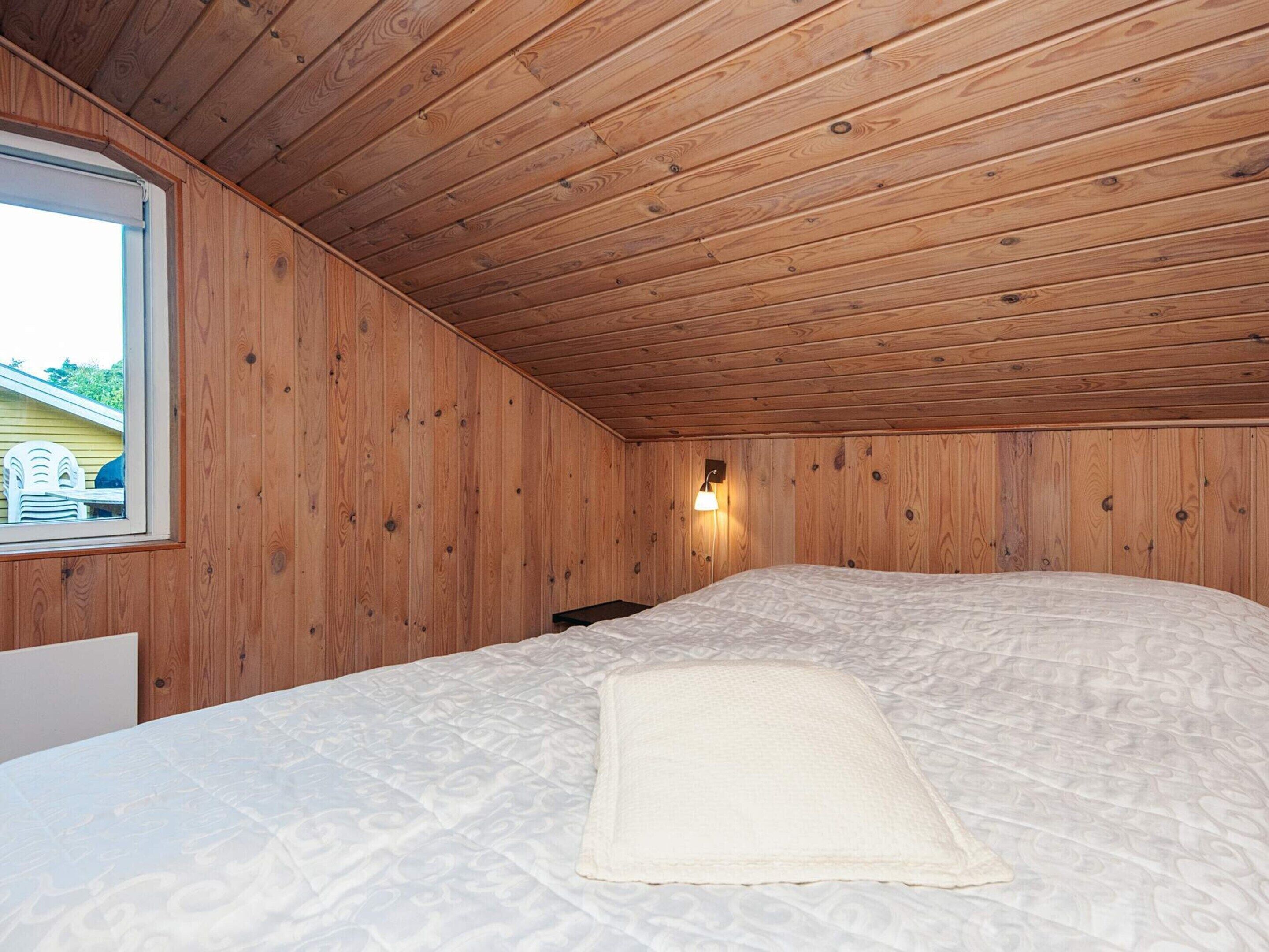 Una habitación con paneles de madera, una cama con colcha blanca y una ventana con vista a un edificio amarillo.