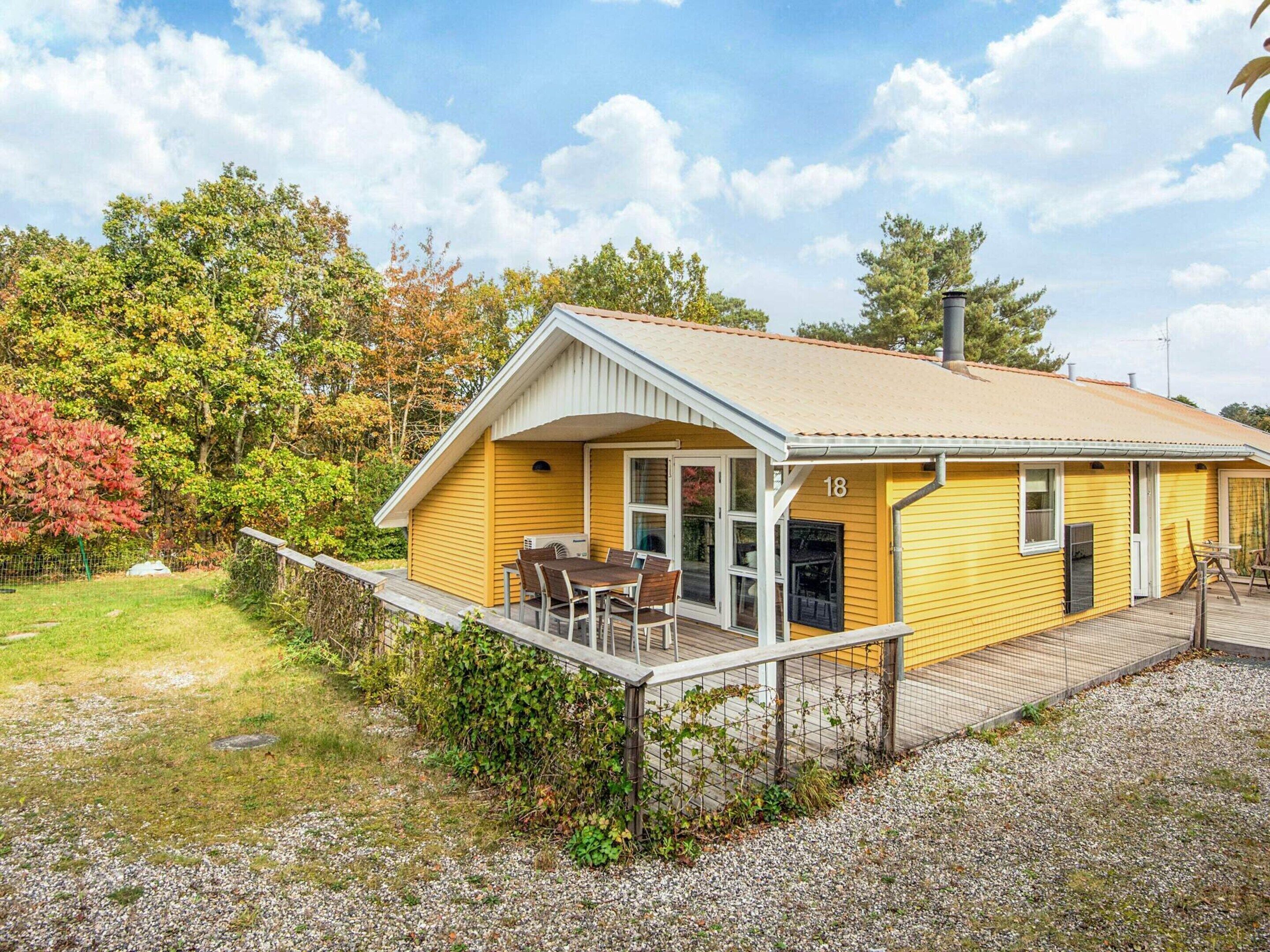 Ein gelbes Einfamilienhaus mit Veranda, Hinweisschild mit der Nummer 18 und einer kleinen Terrassenfläche.