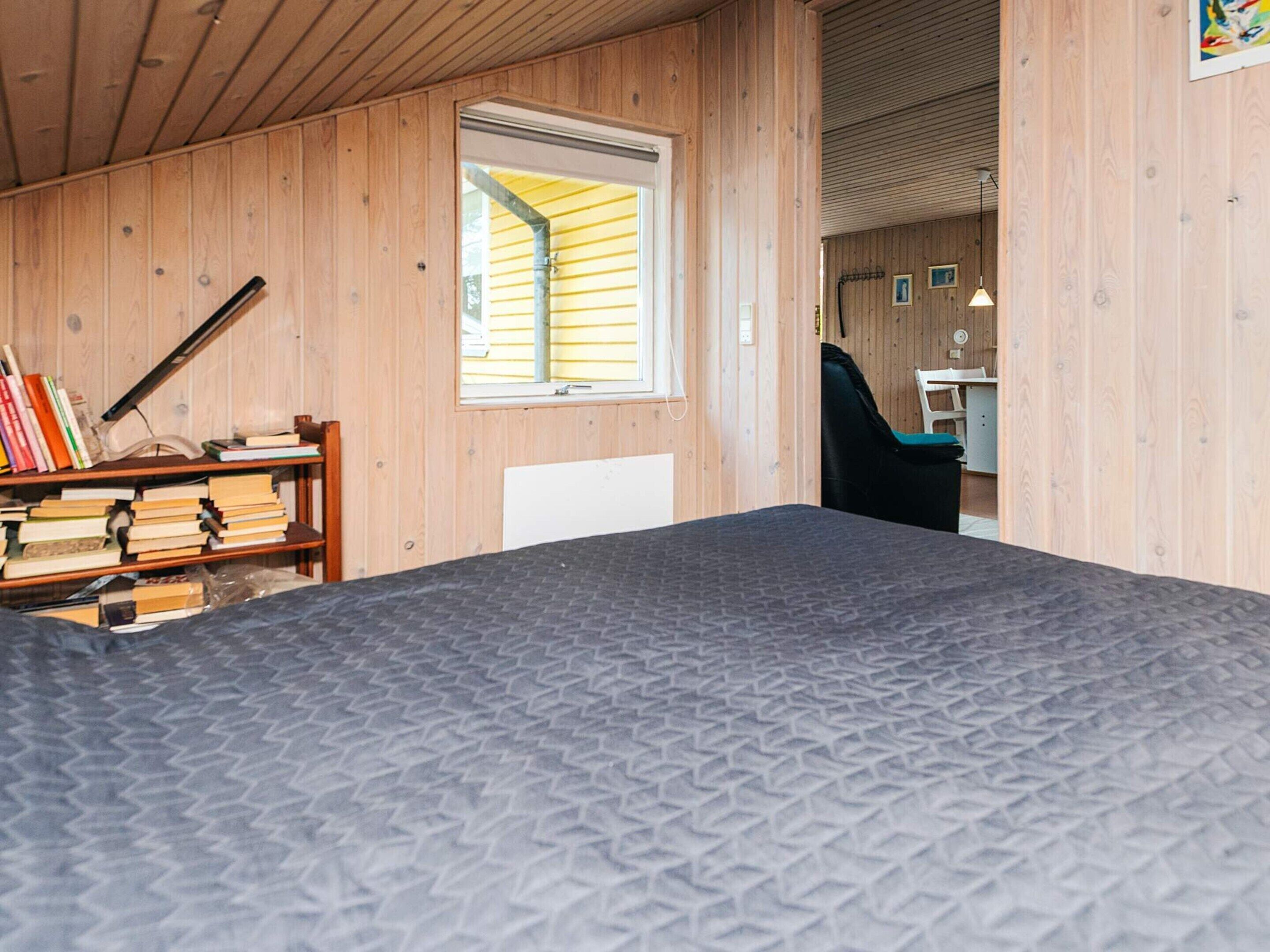 A room with a bed, a desk with books, a window, and a chair.