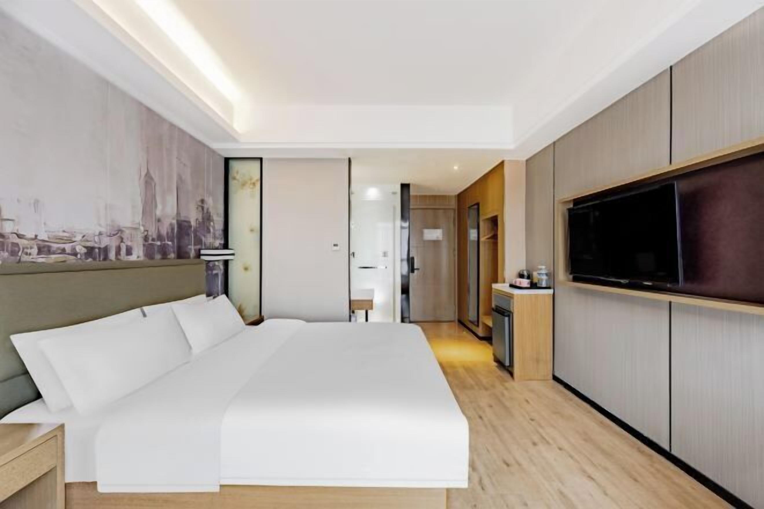 A modern hotel room with a large bed, a flat-screen TV, and a cityscape mural on the wall.