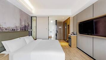 A modern hotel room with a large bed, a flat-screen TV, and a cityscape mural on the wall.