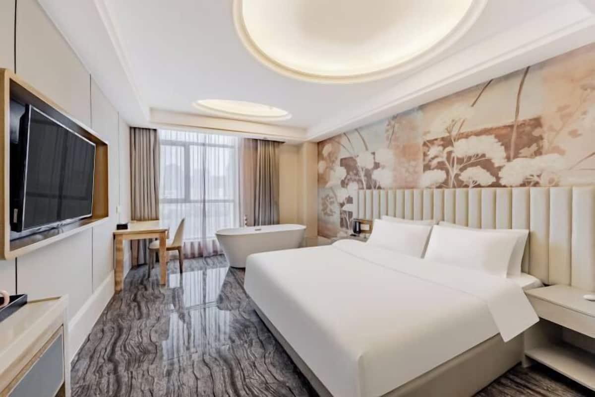 A modern hotel room with a large bed, a flat-screen TV, a desk, and a bathtub.