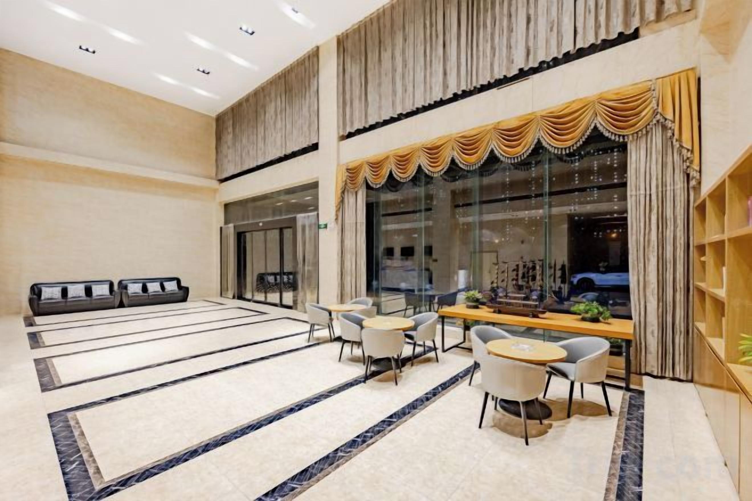 A spacious lobby with a reception desk, seating area, and a large window with curtains.
