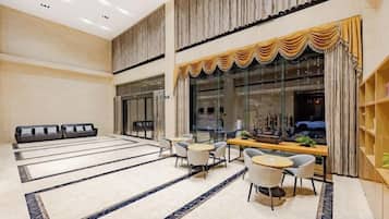 A spacious lobby with a reception desk, seating area, and a large window with curtains.