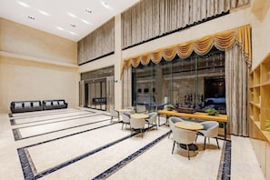 A spacious lobby with a reception desk, seating area, and a large window with curtains.
