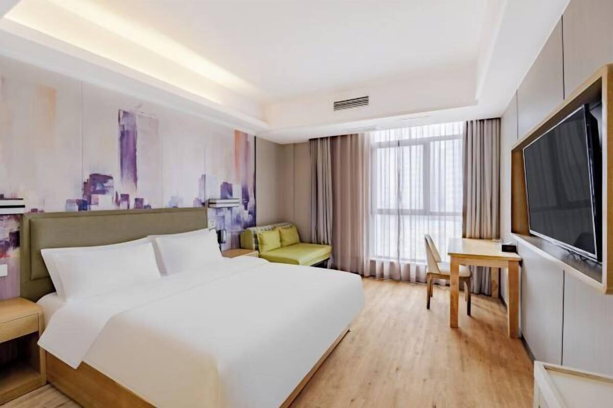A hotel room with a large bed, a desk, a chair, a TV, and a window with curtains.