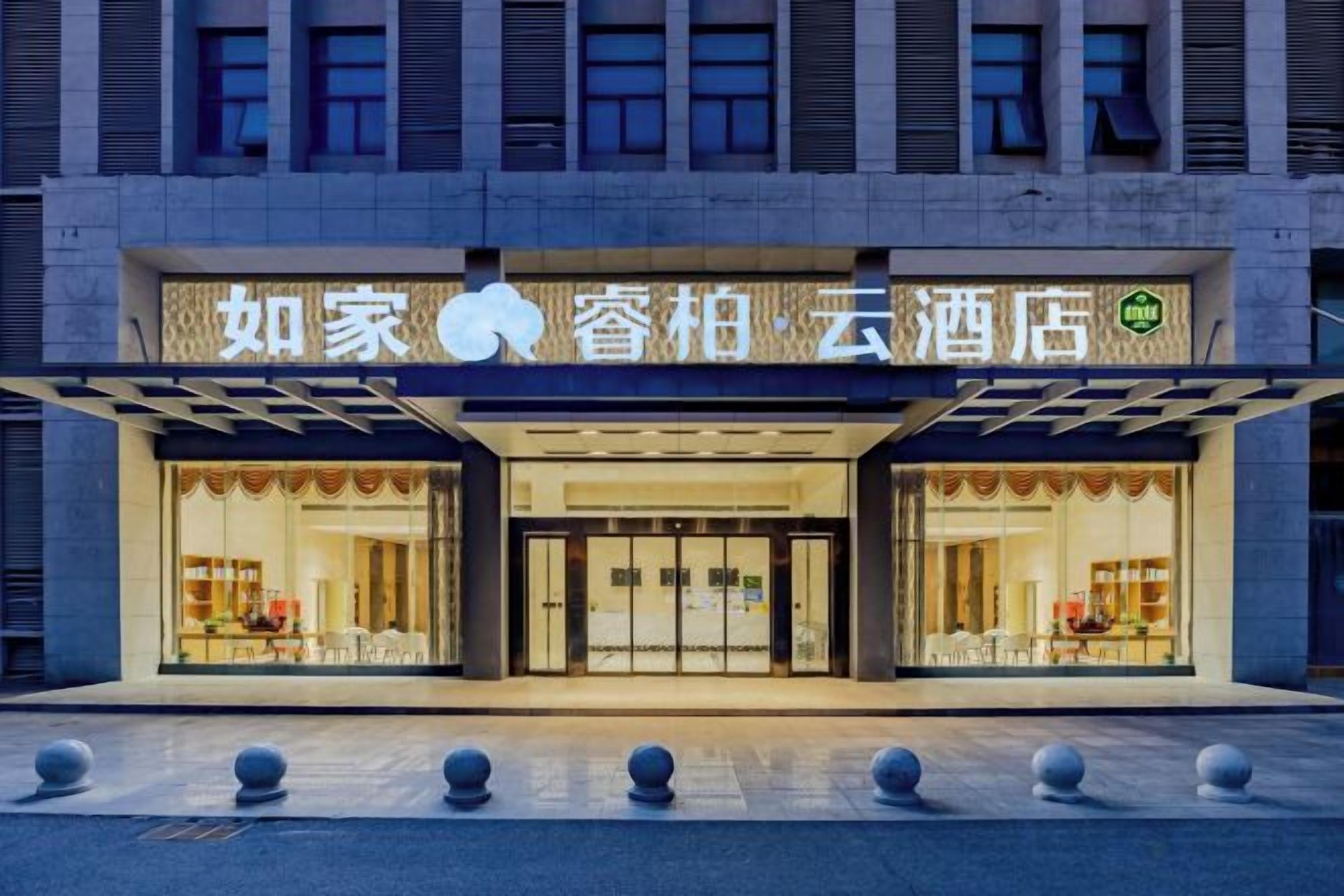 A hotel entrance with a sign, glass doors, and a covered walkway.
