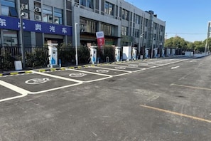 Un estacionamiento con estaciones de carga para vehículos eléctricos, un edificio con señalización y un cielo despejado.