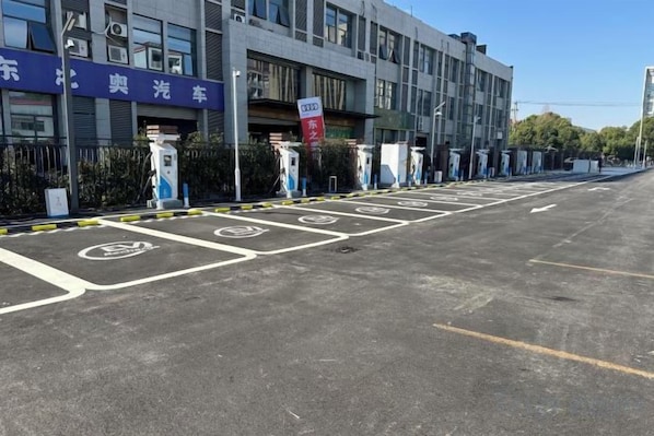 A parking area with electric vehicle charging stations, a building with signage, and a clear sky.
