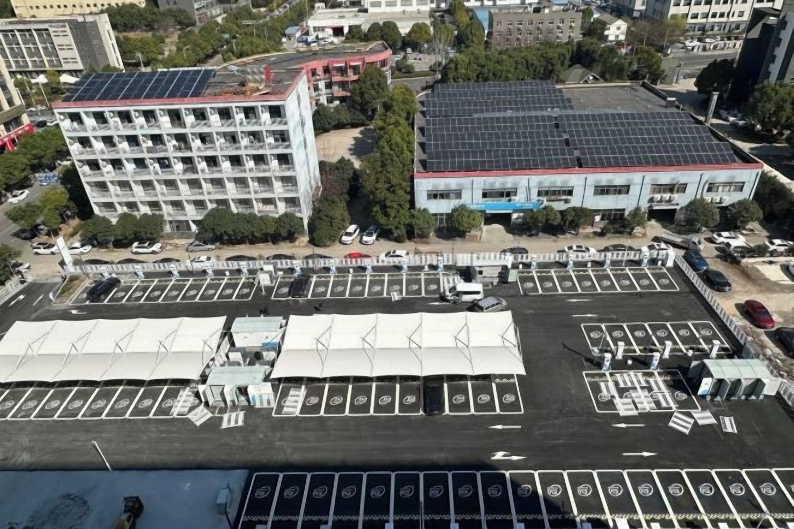 Un estacionamiento con varias filas de espacios, un edificio con techo solar y una gran estructura tipo carpa.