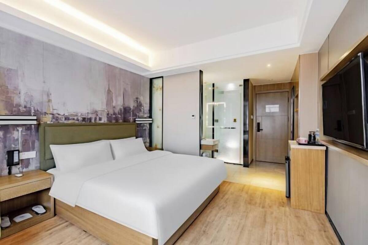 A modern hotel room with a large bed, a television, a nightstand, and a cityscape mural on the wall.