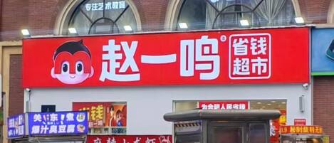 A red storefront with a cartoon character logo, a blue signboard, and a small kiosk.