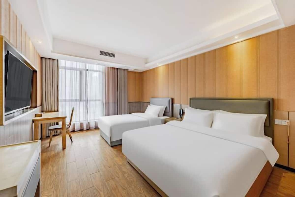 A hotel room with two beds, a TV, a desk, and a window with curtains.