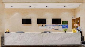 A reception desk with a marble counter, two monitors, and a plant.