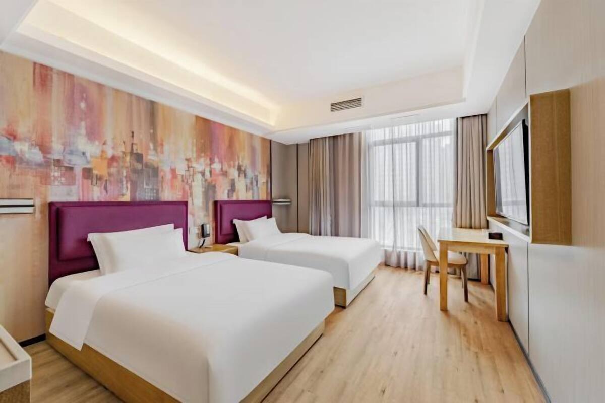 A hotel room with two beds, a desk, a chair, a TV, and a large abstract painting on the wall.