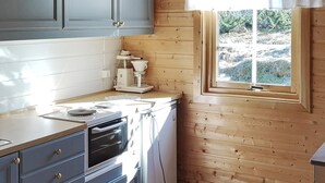 Ett kök med träpanel på väggarna, ett fönster med en vit gardin och en kaffebryggare på bänkskivan.