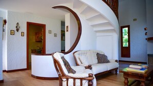 A spacious living room with a curved staircase, a sofa, a wooden chair, and a small table with books. - Al Martinitt by Wonderful Italy (Bellagio)