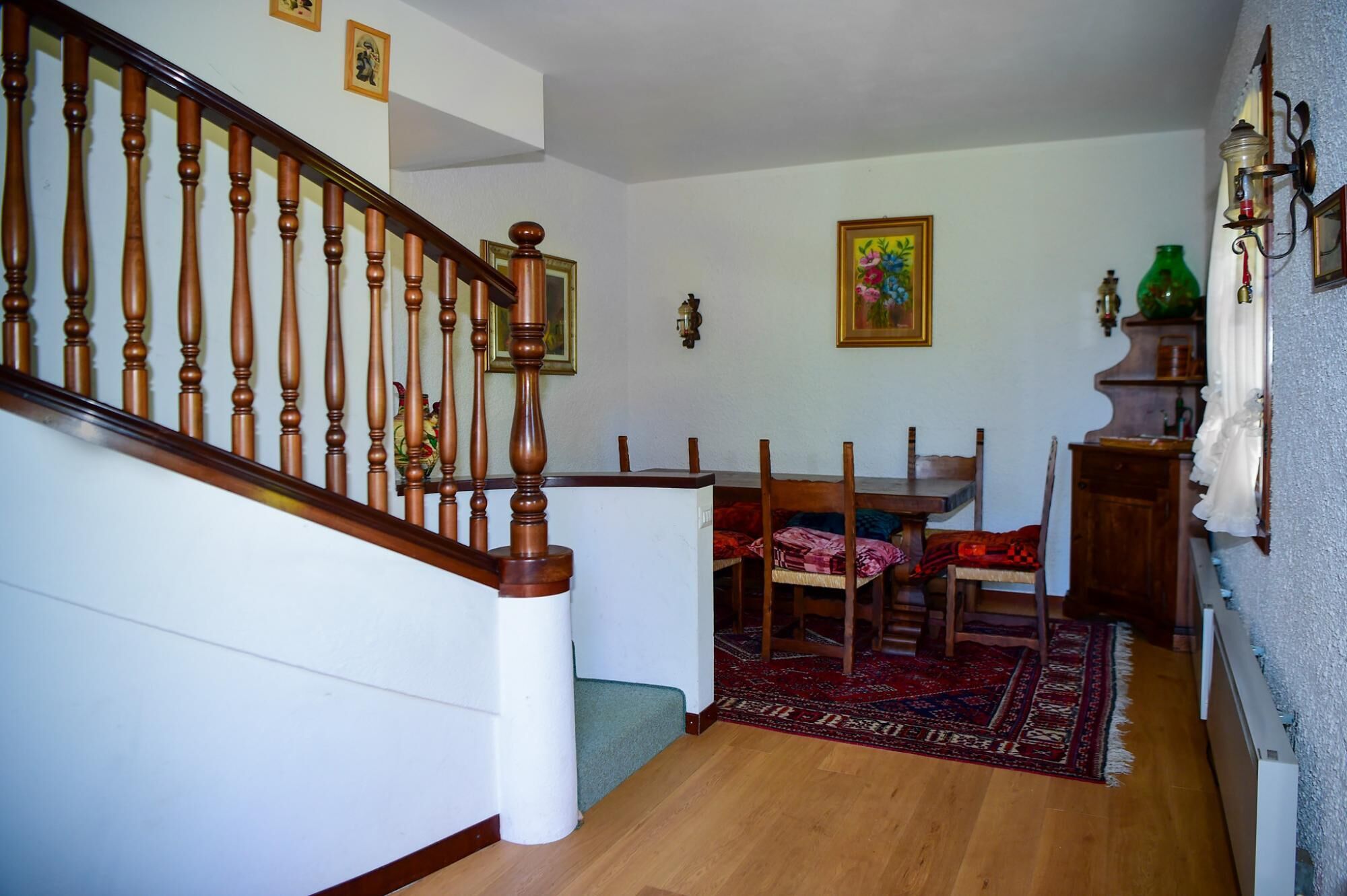 Una scala con ringhiere in legno conduce a una sala da pranzo con tavolo e sedie.