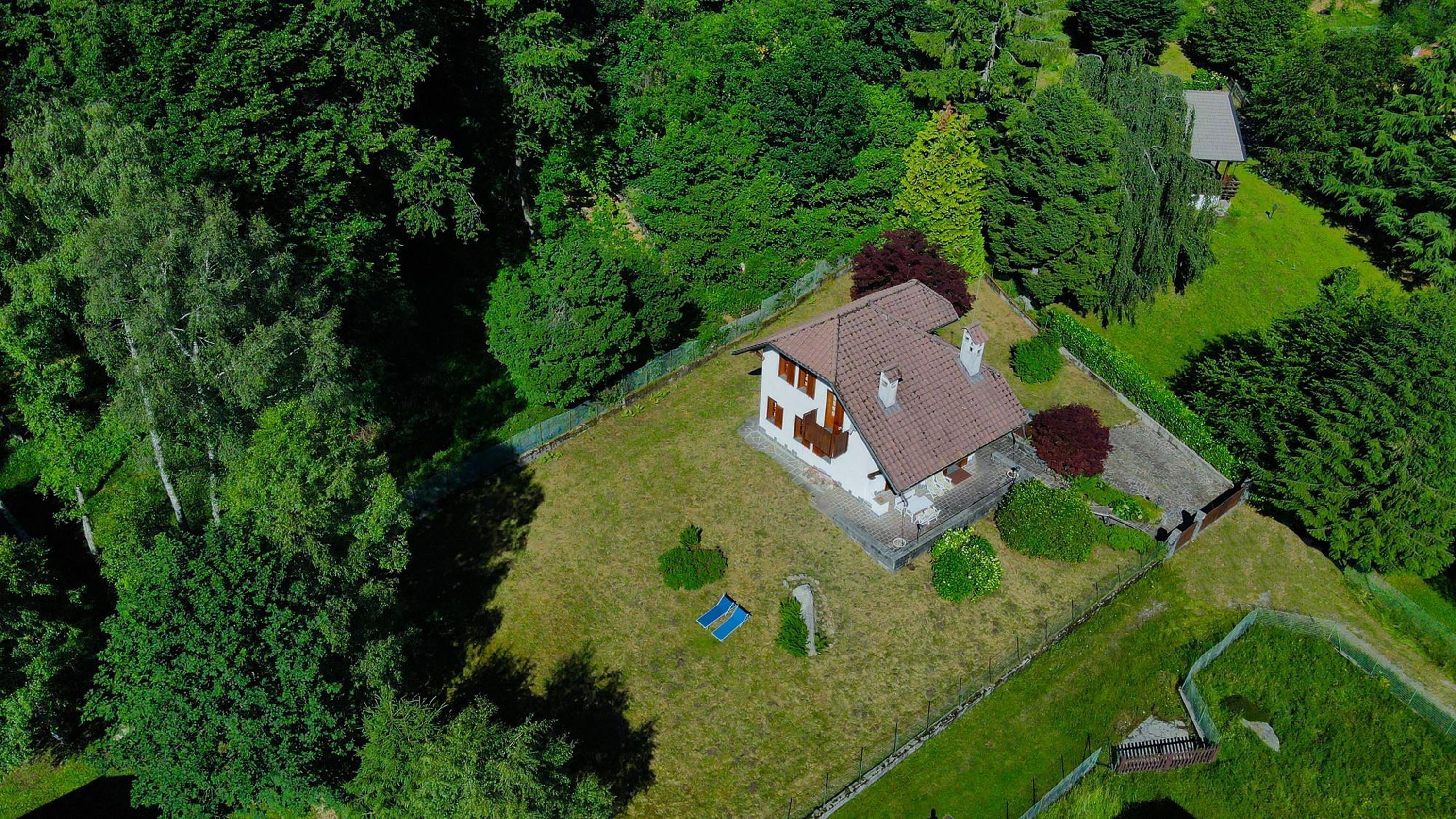 Vista aérea de una casa rodeada de un bosque frondoso, con un pequeño jardín y un objeto azul en el césped.