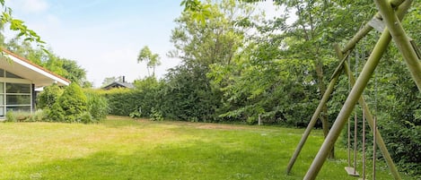 A grassy backyard with a swing set and a house in the background.