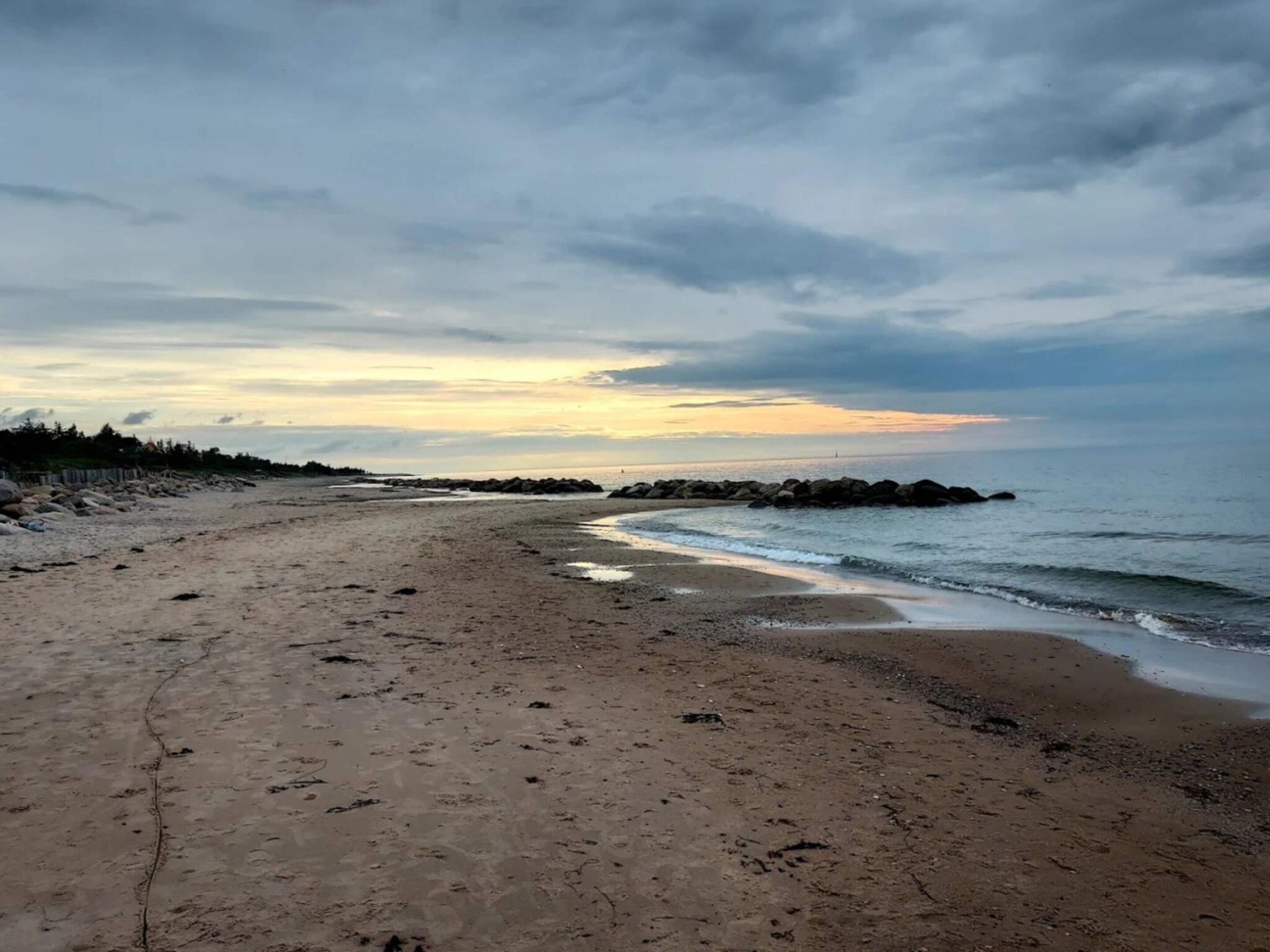 A beach with a rocky shoreline, a clear sky, and a distant horizon.