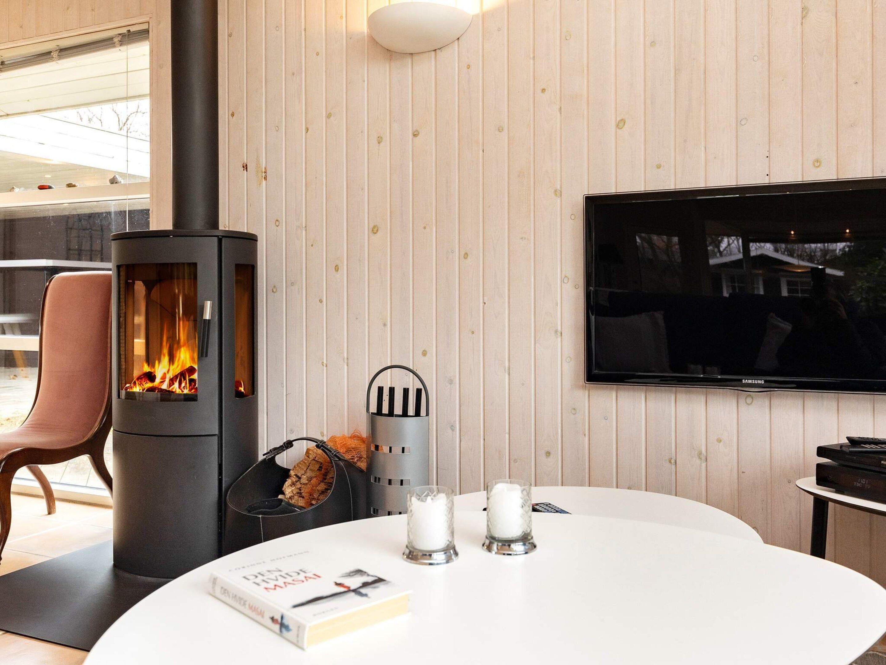 A modern living room with a wood-paneled wall, a fireplace, a flat-screen TV, and a round table with a book and candles.