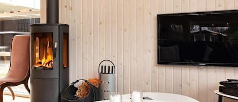 A modern living room with a wood-paneled wall, a fireplace, a flat-screen TV, and a round table with a book and candles.