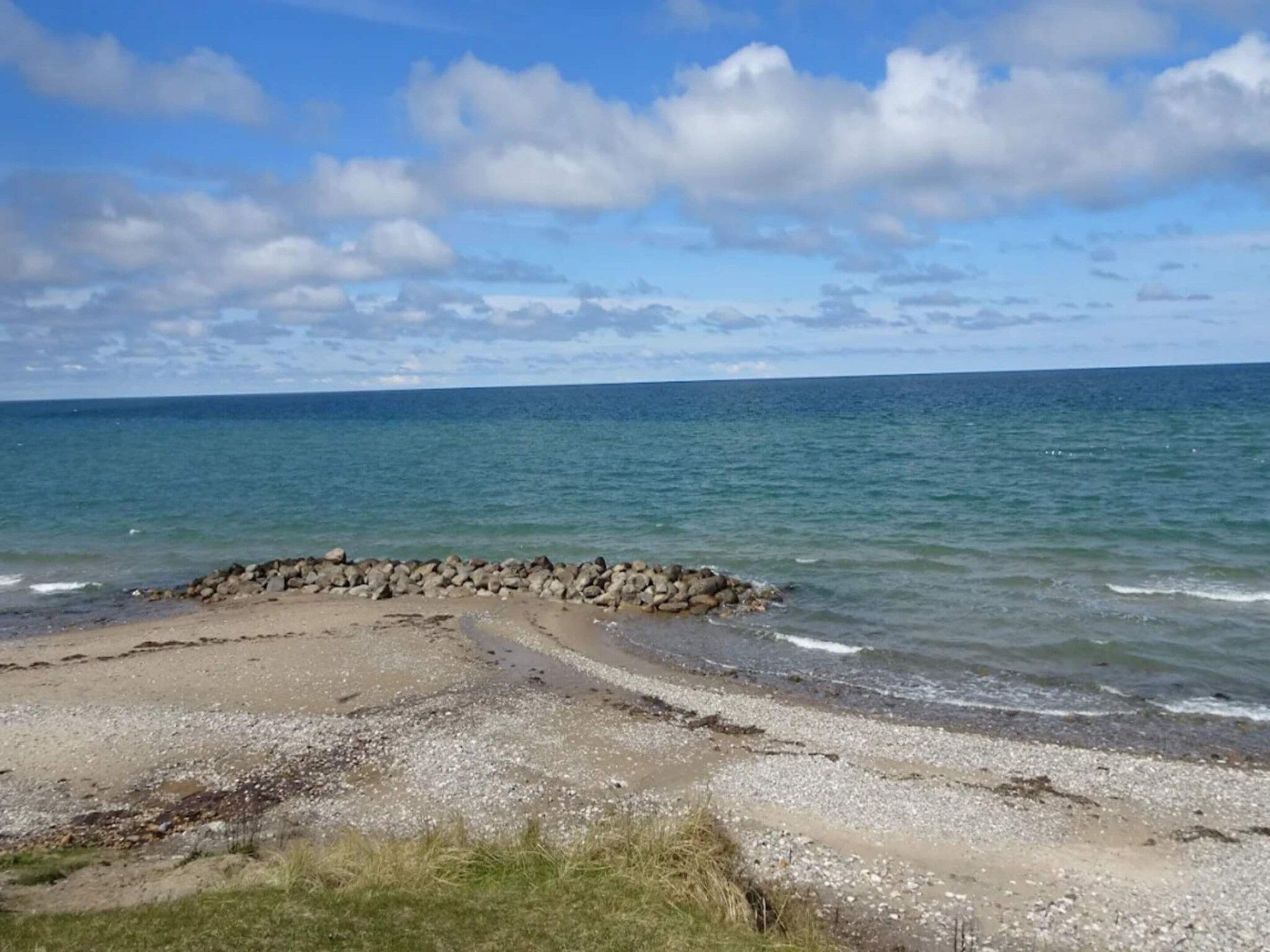 Une plage avec une digue rocheuse, une mer calme et un ciel dégagé.