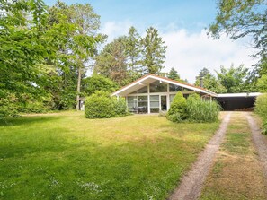 A modern house with a covered patio, surrounded by a well-maintained lawn and dense greenery.